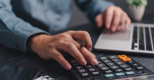 man working out calculations on a calculator and laptop for a pension transfer
