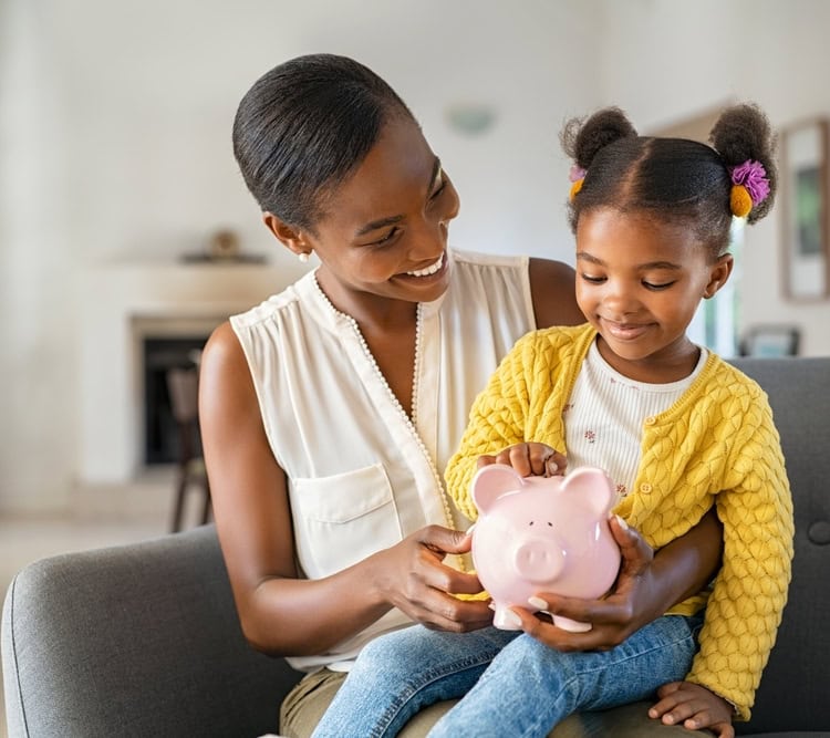 Smiling,Mature,African,American,Mother,Helping,Daughter,Sitting,On,Lap mum and daughter putting money into piggy bank