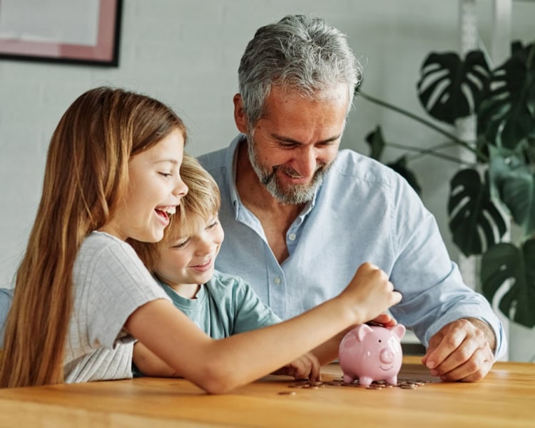 Grandparent,Grandfather,And,His,Grandson,And,Granddaughter,Putting,Coin,Money two children saving money with their dad