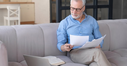 Retirement senior self employed man looking at paperwork and laptop